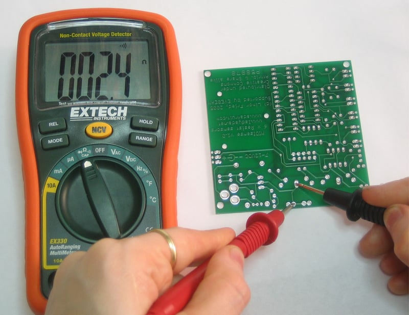 Multimeter probes touching two circuit-board points; the display shows ohms.
